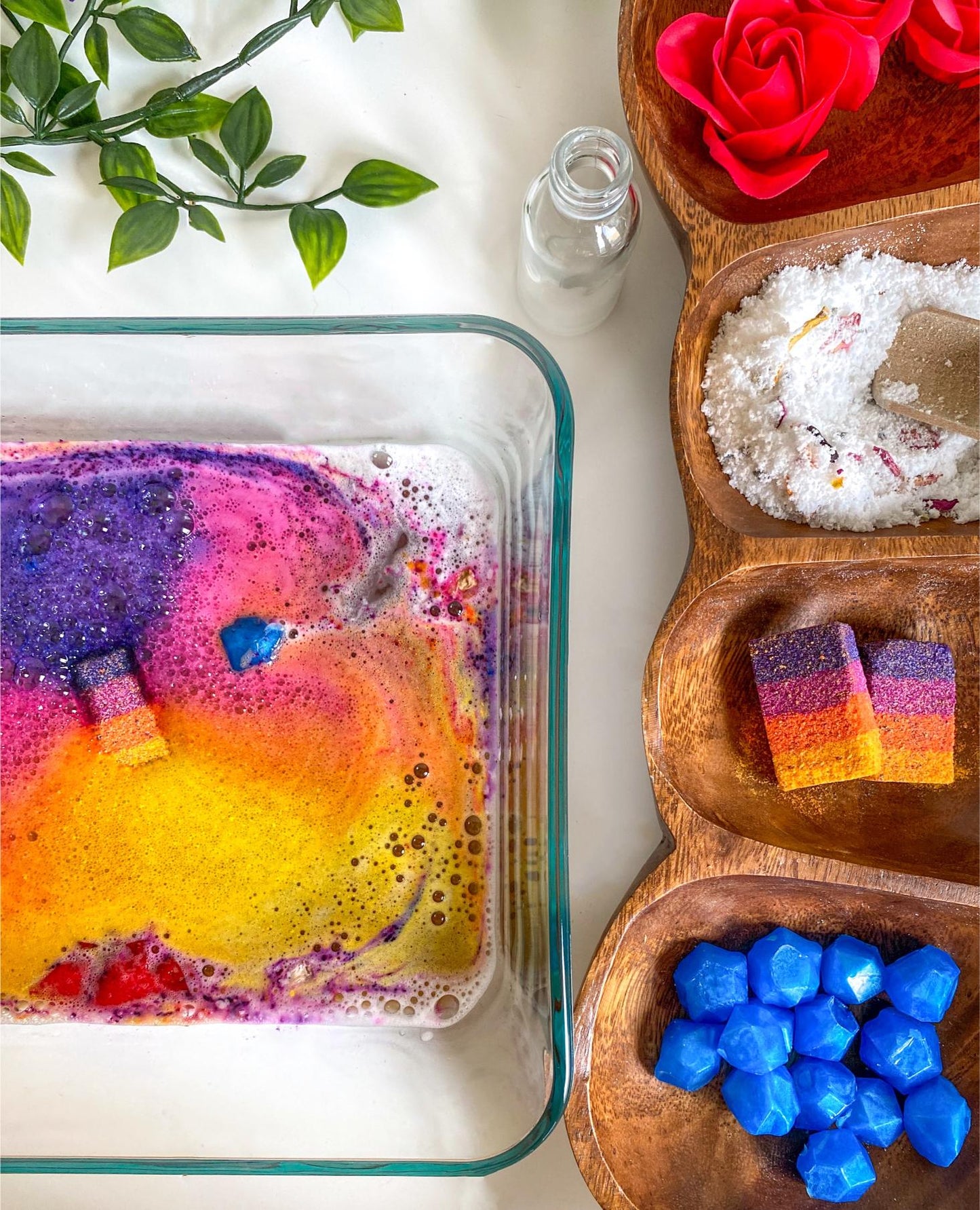 Close-up of a sensory potion kit color-changing bath water swirling in pink, purple, orange, and yellow, with a red rose in bloom and a blue gem-shaped melt floating on the surface